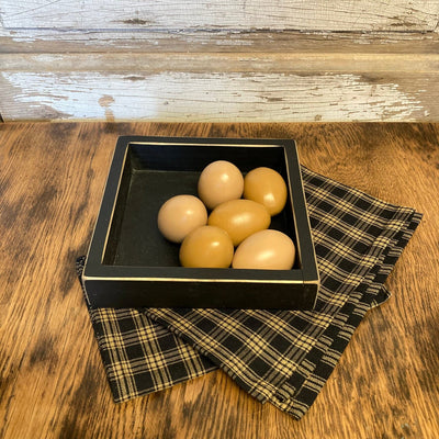 Six resin eggs in a black wooden box on a plaid cloth with a wooden background
