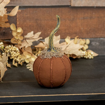 Decorative brown fabric pumpkin with a textured surface on a dark surface with gold leaves and berries.