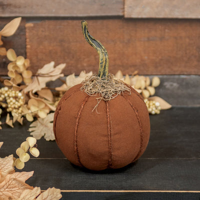 Orange Brown fabric pumpkin with a brown stem on a wooden surface with decorative leaves.