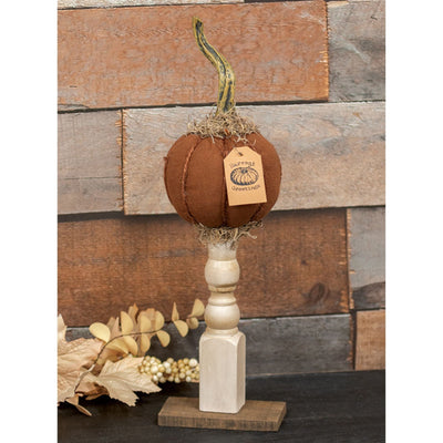 Decorative orange fabric pumpkin on a cream wood stand with a wooden background